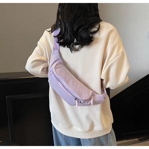 Detail of lavender nylon sling bag showing adjustable strap and minimalist zipper on model