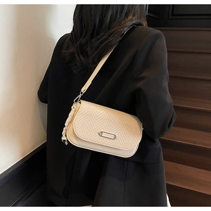 Détail du sac bandoulière avec rabat en paille tressée et plaque argentée sur veste noire