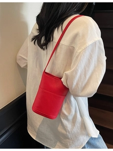Red lychee grain leather bucket bag worn by model in white shirt on a staircase