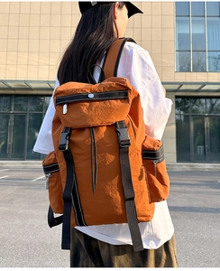 Outdoor view of orange hiking backpack with buckle closure and side zipper pockets