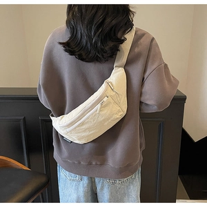 Detail of off-white nylon crossbody chest bag showing zippers and wide strap on a person