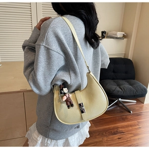 Close-up of cream half-moon bag featuring silver metal lock and pearl doll charm