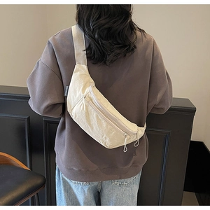 Detailed back view of a beige nylon crossbody bag worn by a model in a minimal setting