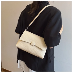 Close-up of a cream-colored textured faux leather shoulder bag with a square buckle