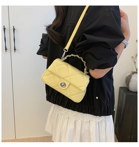Detail of light yellow quilted crossbody bag with gold chain and metal twist lock