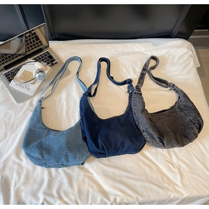Three colors of oversized denim hobo bags with adjustable straps on a soft white bed