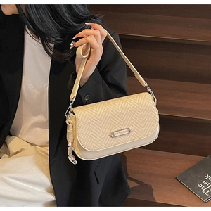 Détail d'un sac à main beige avec rabat tissé et plaque en métal sur un escalier