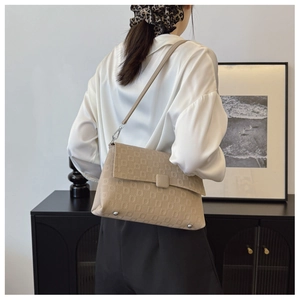 Detail of beige underarm bag with geometric embossing and silver hardware on a model