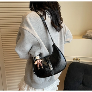 Detail of a black pleated leather crescent hobo bag with silver lock and a cute doll charm