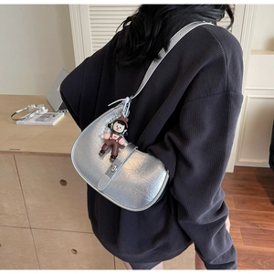 Close-up of silver crescent handbag featuring pleated leather texture and cartoon pendant