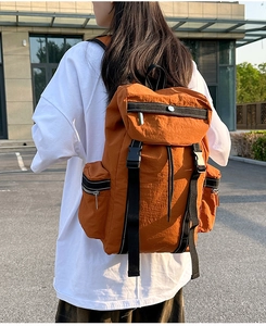 Outdoor shot of an orange hiking backpack with multiple zipper pockets and buckles