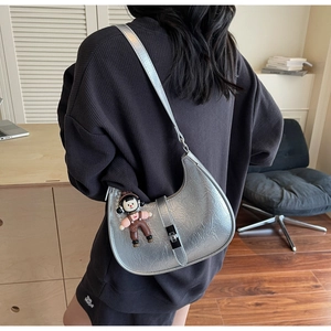 Side view of silver quilted crescent bag on model with cute doll pendant detail