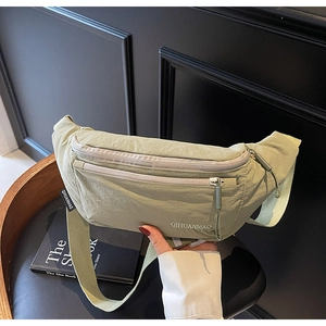Detail of sage green nylon sling bag showing zipper pockets and adjustable woven strap