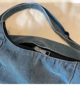 Detail of smooth metal zipper and premium blue denim texture on casual crossbody bag