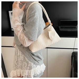 Detail of cream woven tote bag with braided shoulder strap shown in a modern office setting