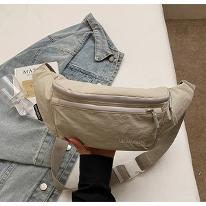 Detail of adjustable strap and zipper on beige nylon crossbody sling bag with brand logo