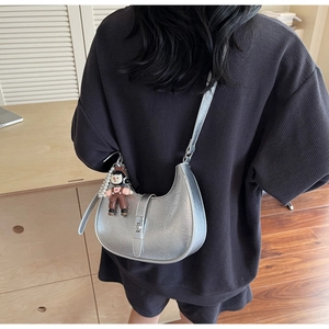 Detail view of a silver pleated half-moon crossbody bag with a cute cartoon character charm