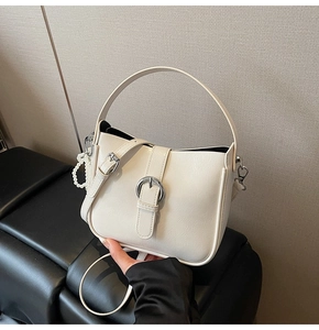 Detailed view of white bucket bag featuring silver buckle and elegant pearl chain accessory