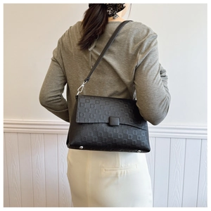 Detail of black leather underarm bag featuring embossed pattern and metal bottom studs