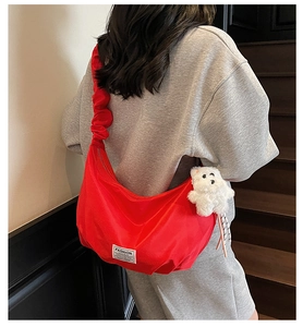 Detail of red nylon crescent bag with ruched strap and cute teddy bear pendant