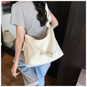 Détail de la bandoulière froncée et lettrage brodé sur le sac cabas en nylon beige