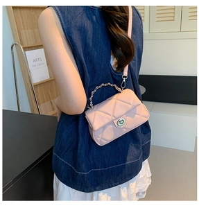 Detail view of a pink quilted crossbody bag with metal chain strap worn by a model