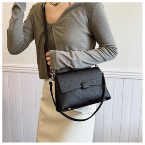 Detail of black pebbled leather crossbody bag with embossed monogram flap and silver hardware