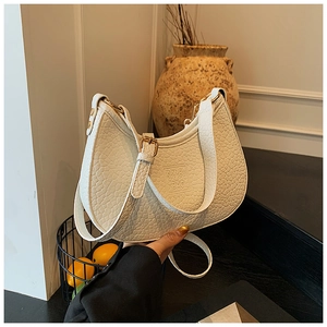 Detail of white half-moon bag featuring grainy texture and gold metallic hardware accents