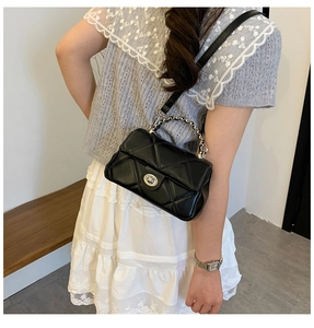 Detail of black quilted crossbody bag with silver twist lock and chain strap on model