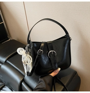 Detail of black glossy shoulder bag with silver buckle and pearl bow charm accessory