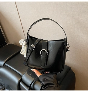 Detail of black glossy bucket bag with silver buckle and elegant pearl lace charm