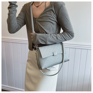 Detail view of light grey shoulder bag featuring geometric square texture and flap closure