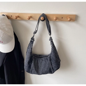 Detail of washed denim half-moon dumpling bag with wide shoulder strap and zipper