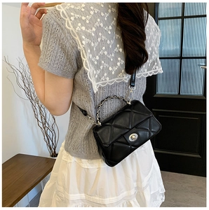 Detail of black quilted leather shoulder bag with silver turn-lock and chain handle
