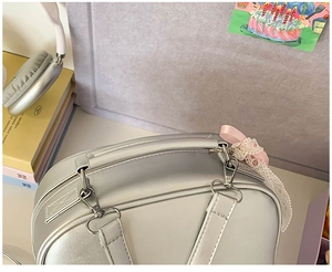 Détail du sac à main argenté avec nœud en soie rose et décoration en dentelle blanche