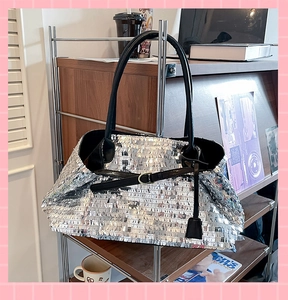 Close-up of a silver sequined tote bag featuring black shoulder straps and metal buckle detail