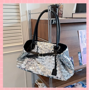Macro view of a large silver sequin tote bag with black leather straps and buckle details