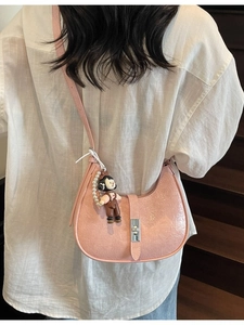 Pink crescent crossbody bag with glossy texture and pearl charm on a stylish model