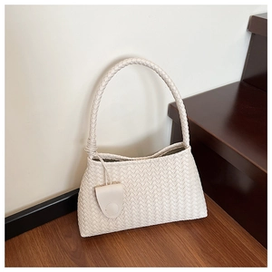 Detail of beige woven hobo bag showing intricate texture and oval charm on a wooden staircase