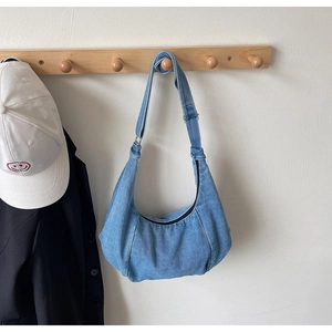 Detail of light blue denim crescent bag hanging on a hook in a minimalist home setting