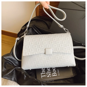 Detail shot of the quilted geometric pattern and silver buckle on a gray shoulder bag