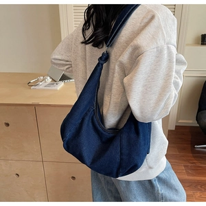 Detail of blue denim hobo bag featuring a decorative knot on the shoulder strap