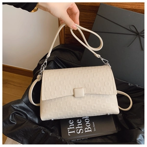 Close-up of beige textured underarm bag with silver square buckle and metal rivets