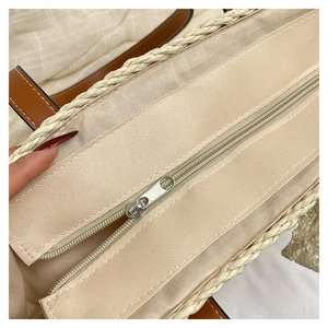 Detail of silver zipper closure and beige canvas lining inside the woven straw tote bag