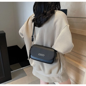 Détail du sac à bandoulière noir avec texture tressée et plaque en métal de mode