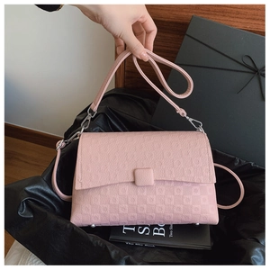 Detail view of pink embossed crossbody bag with square buckle and protective metal feet