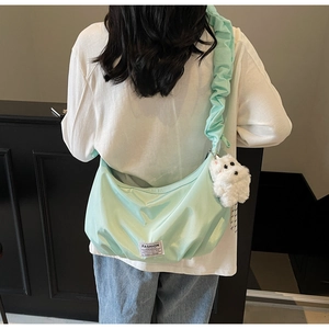 Detail of mint green hobo bag with ruffled strap and plush dog charm on a model