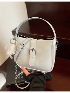 Elegant minimalist shoulder bag with silver buckle and pearl pendant on wooden stairs