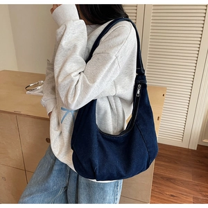 Detail of a dark blue denim hobo bag worn over the shoulder with a minimalist lifestyle backdrop