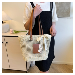 Detail of hollow-out straw tote bag with brown leather handles and white lace bow decoration